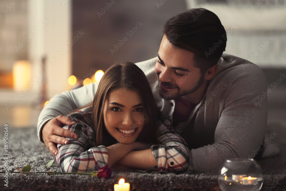 Happy young couple lying on floor in room with burning candles