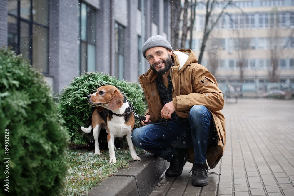Handsome young hipster walking his dog outdoors on snowy day