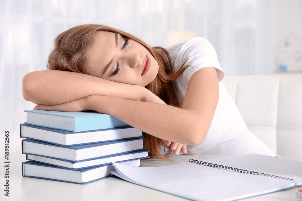 Tired student sleeping on stack of books at her desk. Preparing for exam
