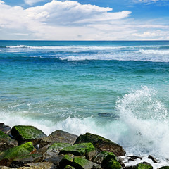 Wall Mural - Waves break against stony shore of ocean.