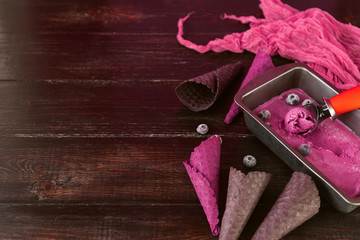 pink ice cream with a spatula for ice cream on a dark wooden background with waffle cups