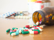 Colorful medicine capsules spilling out of brown glass bottle w/ pharmaceutical medicament on wood table. Drug prescription, treatment of disease, antibiotic resistant problem and health care concept.