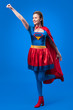 © LIGHTFIELD STUDIOS - smiling woman in superhero costume with outstretched arm isolated on blue