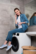 © LIGHTFIELD STUDIOS - cheerful housewife talking on smartphone while sitting on washing machine at home