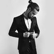 portrait of handsome fashion stylish hipster lumbersexual businessman model dressed in elegant black suit posing on studio background. Metrosexual