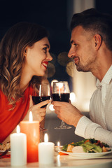 Wall Mural - Young smiling lovers looking at each other and have romantic dinner with wine and food