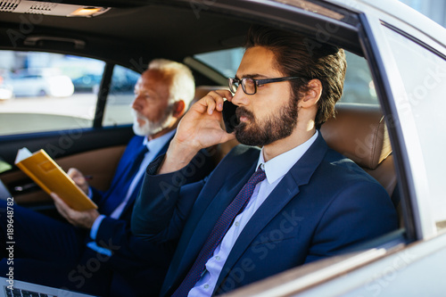 Senior businessman and his assistant sitting in limousine and working Poster Mural XXL
