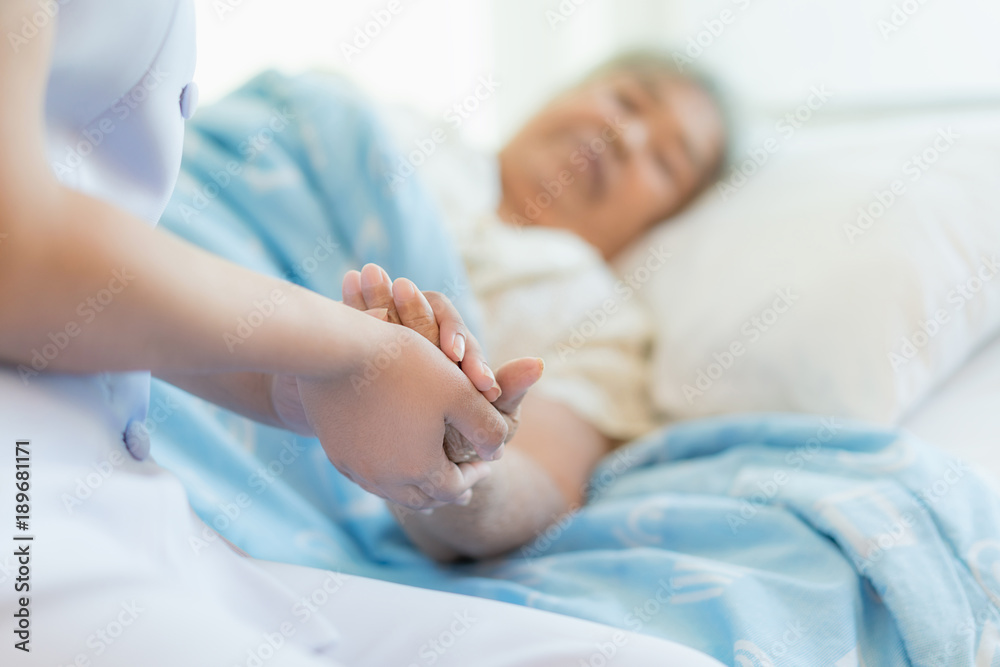 Nurse sitting on a hospital bed next to an older woman helping hands, care for the elderly concept - obrazy, fototapety, plakaty 