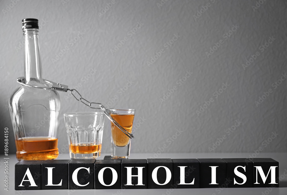 Strong drink, handcuffs and cubes with word ALCOHOLISM on table
