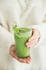 Healthy vegan breakfast. Matcha green smoothie with chia seeds and mint in hands of woman wearing white woolen sweater. Clean eating, vegetarian, alcaline diet, weight loss food concept