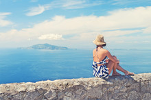 Young Woman Sitting On Wall Looking At Sea And Island
