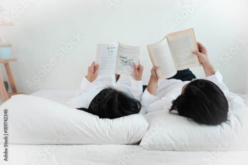 Lovely Couple Reading Book Lying On Bed In Whtie Bedroom