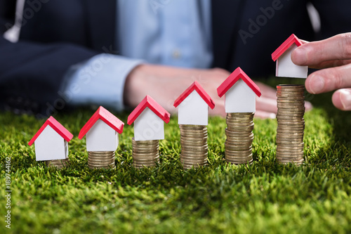 Fotografía Businessperson Arranging House Model Over Stacked Coins