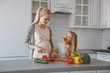 © LIGHTFIELD STUDIOS - daughter eating vegetables while pregnant mother cooking at kitchen