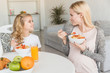 © LIGHTFIELD STUDIOS - smiling mother and daughter eating oatmeal with fruits in morning