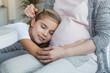 © LIGHTFIELD STUDIOS - cropped image of cheerful daughter sleeping on pregnant mother belly