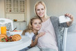 © LIGHTFIELD STUDIOS - smiling pregnant mother and daughter taking selfie in kitchen