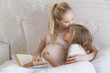 © LIGHTFIELD STUDIOS - pregnant mother kissing daughters forehead and holding book