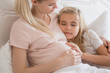 © LIGHTFIELD STUDIOS - happy daughter lying on pregnant mother shoulder in bed
