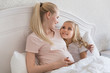 © LIGHTFIELD STUDIOS - smiling pregnant mother and daughter lying in bed