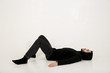 attractive young man with a small beard in black clothes with a hood on his head lies on his back on the floor with his legs bent at the knees and looks at the ceiling