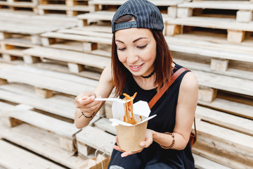 Wall Mural - Beautiful woman student eating asian fastfood from paper box with Delicious chinese Wok noodles