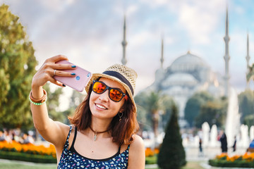 Wall Mural - Happy woman in hat and sunglasses making selfie by the smartphone on the background of the Blue Mosque, Istanbul, Travel and vacation in Turkey concept