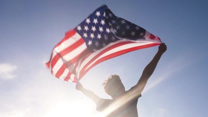 Wall Mural - Young man holding american national flag to the sky with two hands at the beach at sunset usa