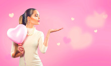Valentine's Day. Beauty Girl With Pink Heart Shaped Air Balloon Pointing Hand, Blows Hearts On Pink Background