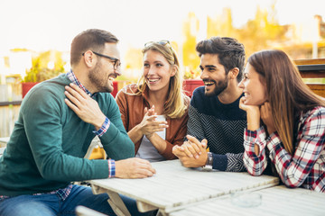 group of four friends having fun a coffee together. two women and two men at cafe talking laughing a