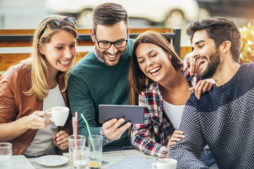 Wall Mural - Group of four friends having fun a coffee together. Two women and two men at cafe talking laughing and enjoying their time