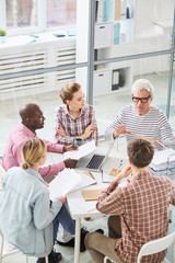 Group of contemporary office workers sitting in circle during start-up meeting and listening to speaker