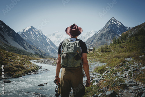 Fotomural A traveler with a backpack stands with his back against the backdrop of the moun