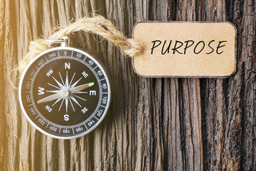 magnetic compass and paper tag written with purpose on old wooden background.