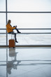 © Yakobchuk Olena - Start of her travel. Full length of young woman with suitcase is looking through window while waiting for boarding at terminal lounge. She is sitting on handrail and drinking coffee. Copy space