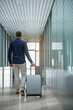 © Yakobchuk Olena - Active lifestyle. Full length back view of elegant traveler is walking along airport hallway with his suitcase