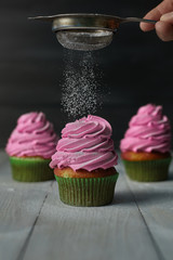 Three pies with pink cream in green paper form for baking sprinkled with powdered sugar on a wooden table