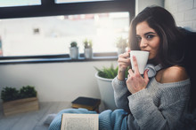 Beautiful Young Woman At Home Drinking Coffee Reading A Book