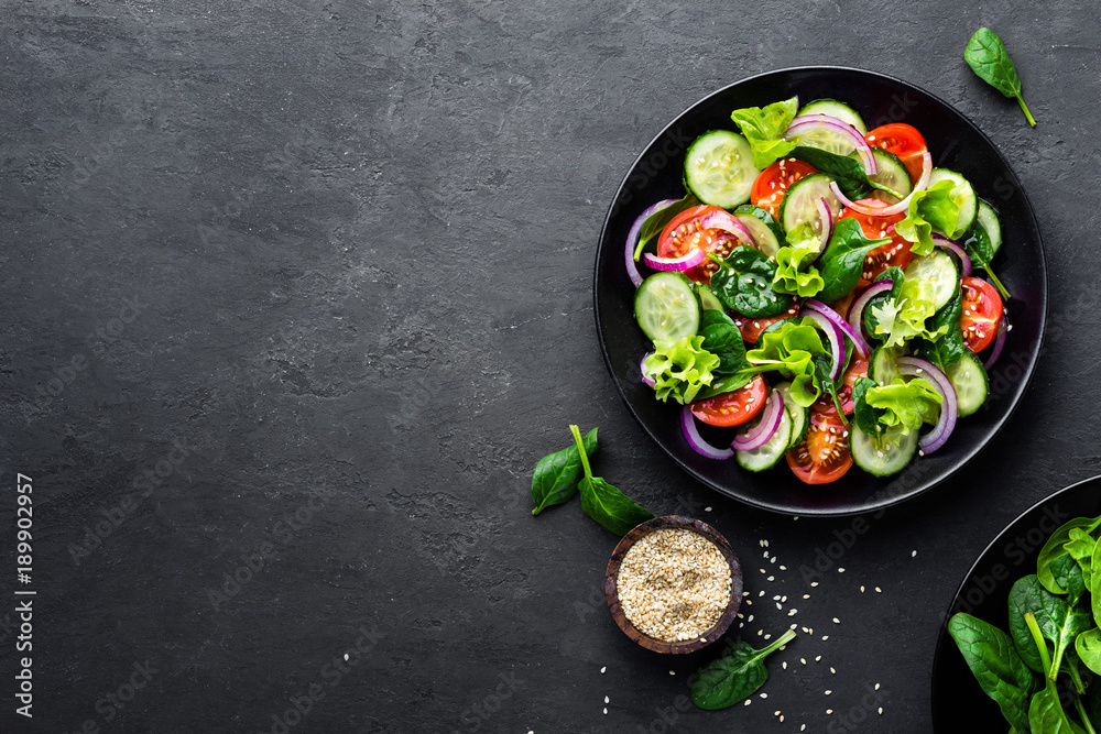Obraz na płótnie Healthy vegetable salad of fresh tomato, cucumber, onion, spinach, lettuce and sesame on plate. Diet menu. Top view. w salonie