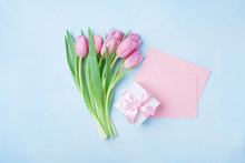 Spring Tulip Flowers, Gift Box And Pink Paper Card On Blue Pastel Table Top View. Greeting For Womans Or Mothers Day. Flat Lay.