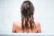 Young girl sitting in bathtub, alone and depressed, back, wet hair 