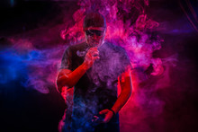 A Man Smokes An Electronic Cigarette. The Man In The Smoke. Bearded Man Vaping. Men With Beard In Sunglasses Vaping And Releases A Cloud Of Vapor. Vaping Man Holding A Mod. A Cloud Of Vapor. 