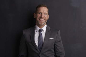 Senior lawyer portrait. Portrait shot of a middle aged businessman with toothy smile looking at camera while standing at dark background. 