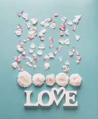 Wall Mural - White word sign LOVE with pale roses and petals on turquoise blue background, top view. Modern minimal flat lay concept