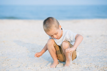 Portrait serious little boy playing in the sand near the sea, ocean. Positive human emotions, feelings, joy. Funny cute child taking vacations and enjoying summer.