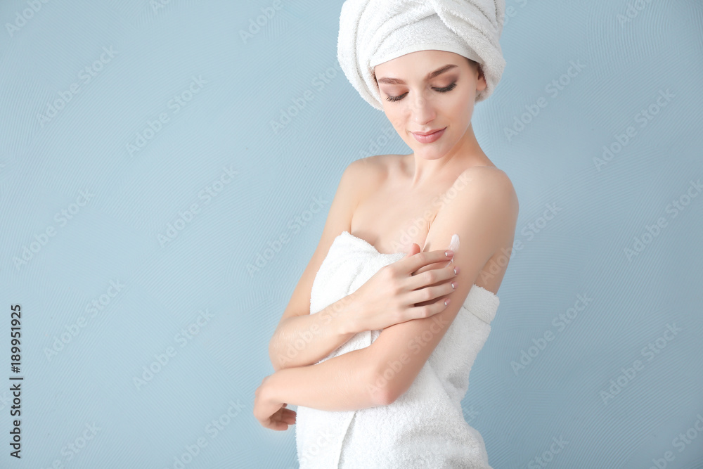 Young woman applying body cream on color background