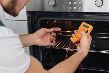 Young man with multimeter repairing oven, closeup