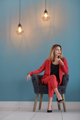 Wall Mural - Beautiful young stylish woman sitting in armchair near color wall