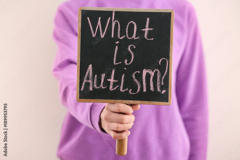 Woman holding chalkboard with phrase "What is autism?" on light background