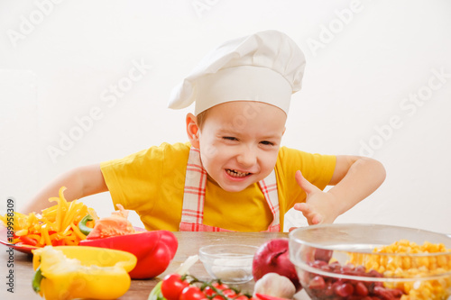 Zdjęcie XXL Zdrowe odżywianie. Szczęśliwe dziecko przygotowuje i zjada warzywa w kuchni